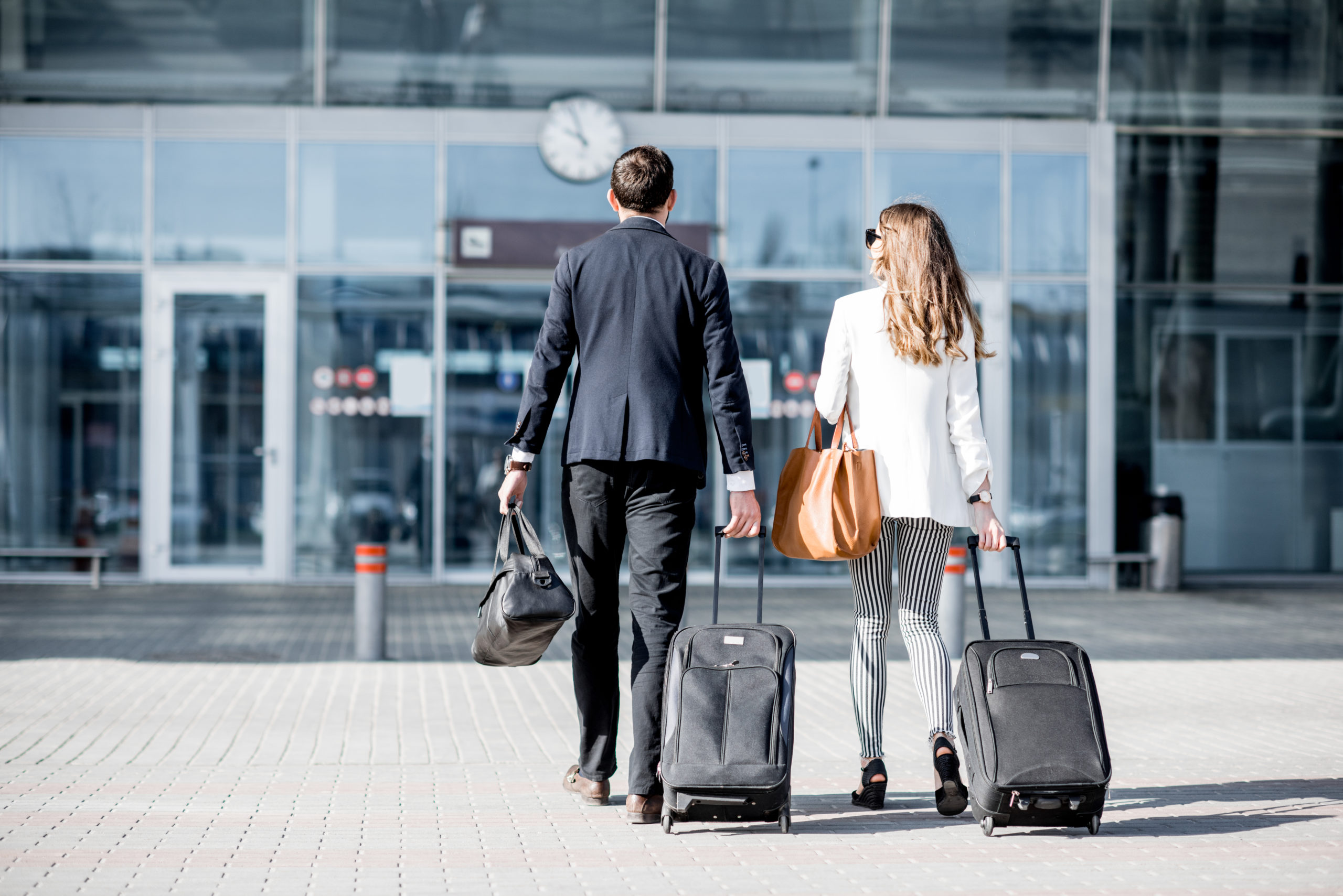 Business,Couple,Walking,Together,To,The,Airport,Entrance,Carrying,Suitcases